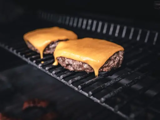 Zwei saftige Burger-Patties auf dem Grill, mit leckerem cheddar schmelzen, der langsam heruntertropft.