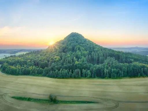 Góry Kaczawskie o wschodzie słońca. Zielony, zalesiony stożek wznosi się nad polami.