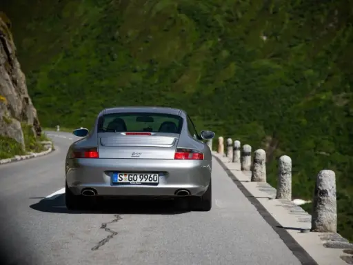 Silberner Porsche 996 4S auf Bergstraße. Ein Klassiker mit Potenzial für Wertsteigerung, der die Freiheit der Fahrt genießt.