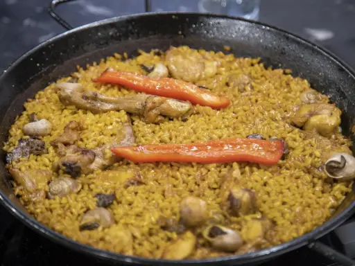 Paella de arroz con carne, pimientos rojos y caracoles. Un plato tradicional español lleno de sabor.