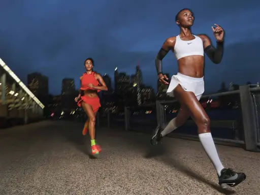Zwei Läuferinnen in sportlicher Kleidung joggen bei Nacht durch eine Stadt. Sie sind motiviert und geben alles, um jeden Tag joggen zu gehen.