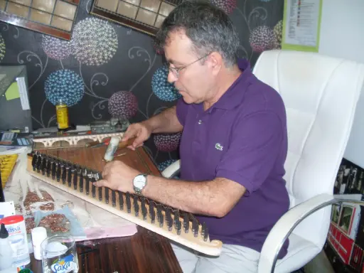Un artisan ajuste les cordes d'un kanun, instrument de musique traditionnel, avec un marteau.