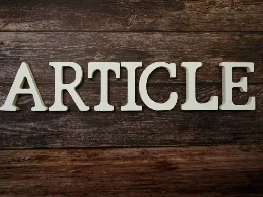 Białe litery układają się w słowo "ARTICLE" na drewnianym tle. To zapowiedź rozszerzonego artykułu po angielsku.