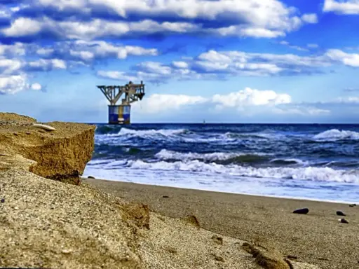 Sandige Klippen am playa del cable, mit einer Plattform im Meer unter dramatischem Himmel.