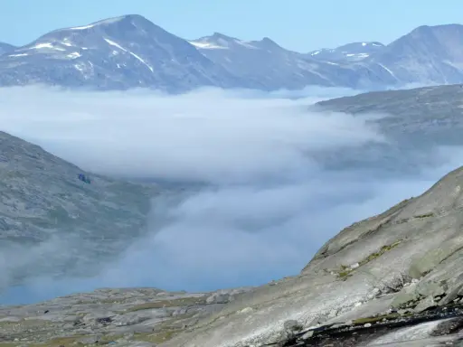 Moln sveper genom dalarna i Padjelanta nationalpark, med snöklädda bergstoppar som reser sig mot en klarblå himmel.