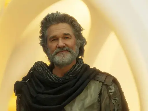 Kurt Russell som Ego i filmer med kurt russell, med grått hår och skägg, klädd i en mörk sjal och rustning mot en gul bakgrund.