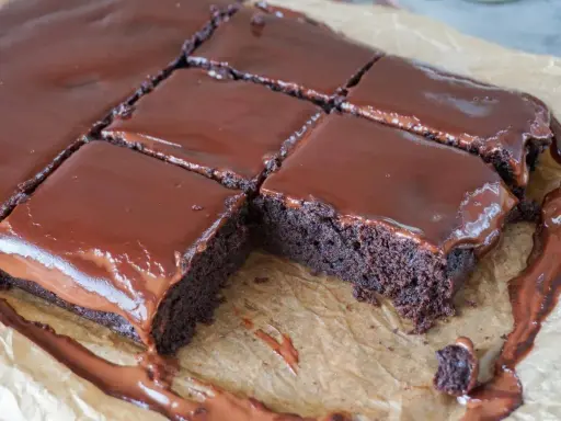 Saftige, vegane Brownies mit glänzendem Schokoladenguss, auf Backpapier zugeschnitten. Ein Traum für jeden Schokoladenliebhaber!
