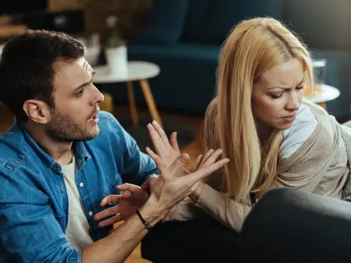 Hombre con expresión de enfado gesticula hacia su pareja, quien lo mira con desprecio, evidenciando una discusión.