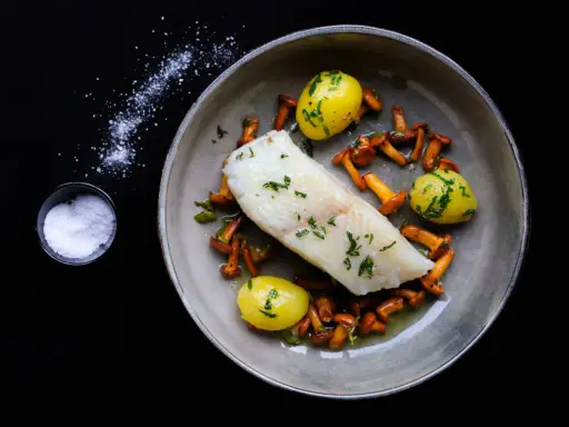 Ein köstliches Heilbutt-Rezept: zartes Fischfilet mit kleinen Kartoffeln und Pfifferlingen, garniert mit frischen Kräutern.