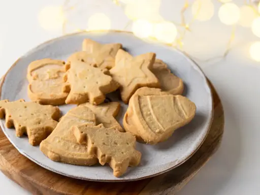 Assortiment de sablés de Noël en forme de sapins, étoiles et cloches, parfaits pour accompagner un chocolat chaud.