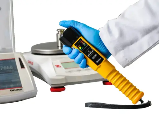 Ręka w rękawiczce trzyma alco sensor 4. Obok wagi laboratoryjne.