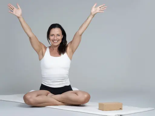 Kvinna i meditationsställning med armarna uppåt, utstrålar lugn och glädje. Hon praktiserar metta meditation för inre frid.