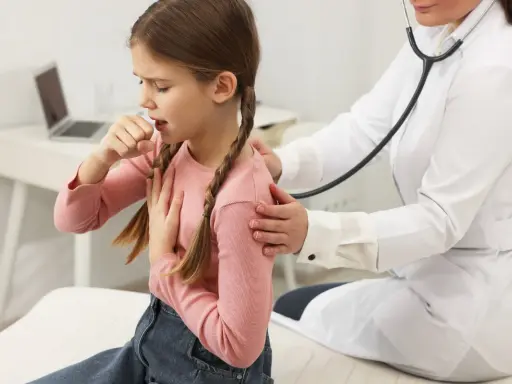 Bambina con trecce tossisce, appoggiando una mano sul petto. Un medico con camice bianco la ascolta con lo stetoscopio, preoccupato per i continui colpetti di tosse bambini.
