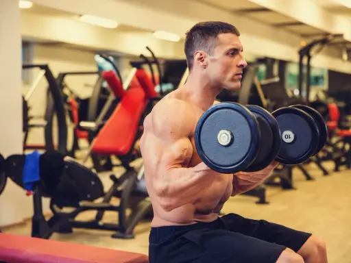 Hombre concentrado realizando ejercicios de bíceps con mancuernas en el gimnasio.