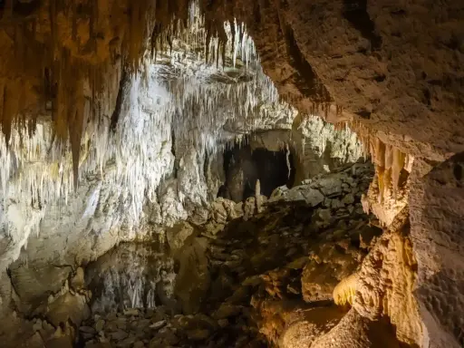 Wnętrze jaskini w Dolinie Kościeliskiej, pełne stalaktytów i stalagmitów. Kamieniste dno i skalne ściany tworzą tajemniczy krajobraz.