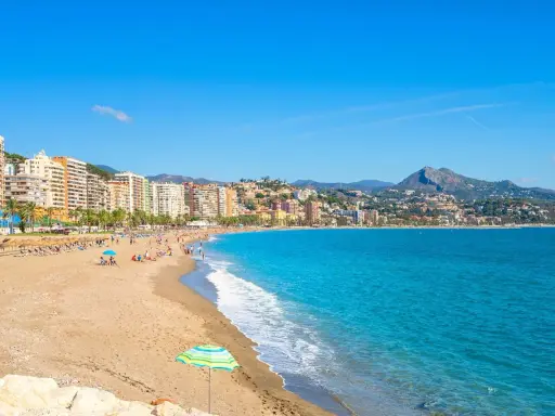 En solig dag på malaga strand med turkost vatten, sand och en stadskant i bakgrunden. En perfekt plats för avkoppling.