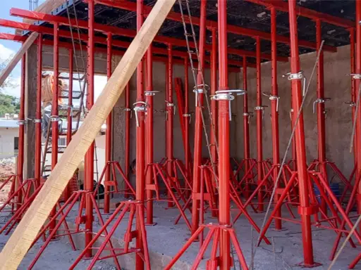 Construcción con varios tipos de puntales rojos sosteniendo una estructura. Un trabajador supervisa.