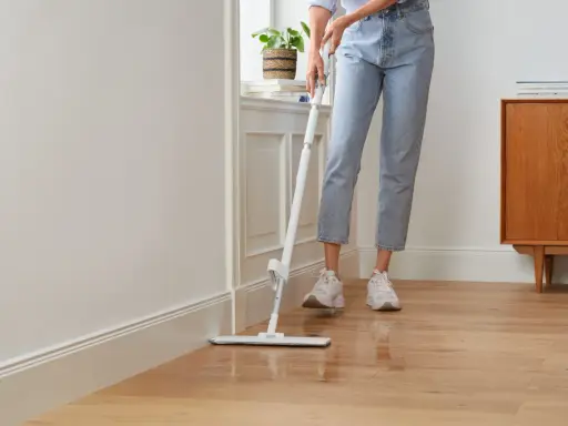 Person wischt den Holzboden, um die Wohnung zu reinigen. Ein moderner Wischmopp gleitet über das glänzende Parkett.