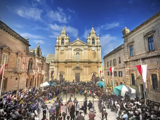 Tłum ludzi w historycznych strojach zgromadzony na placu przed katedrą w Mdina, Malta.