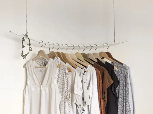 Eine minimalistische **Kapsel Garderobe** mit hellen, gemusterten und erdigen Kleidungsstücken, die an einem Ast hängen.