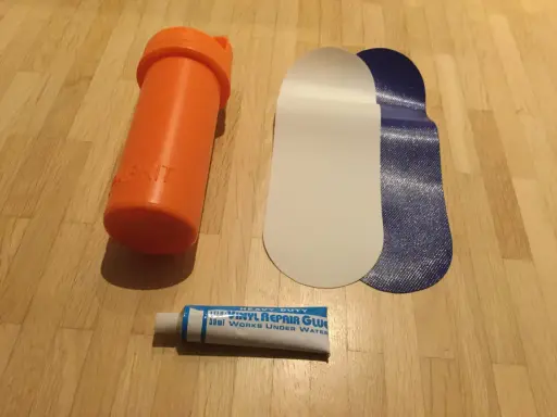 Reparaturset für Schlauchboote: Kleber, Flicken und eine orangefarbene Aufbewahrungsdose.