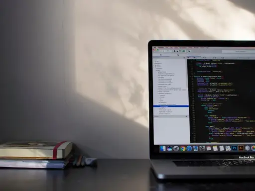 Laptop z kodem w języku C#, gdzie pętla `while` jest kluczowa. Obok leżą notatniki i ołówki.