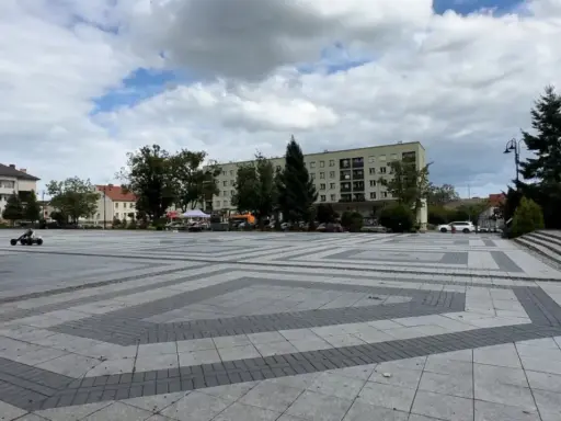 Dziecko na gokarcie przemierza pusty plac, który może być największym rynkiem w Polsce. W tle budynki mieszkalne i drzewa.
