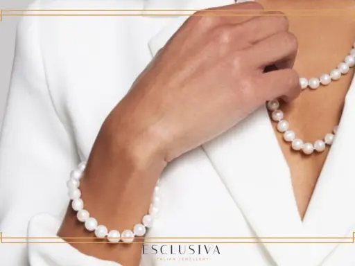Dłoń dotyka naszyjnika z pereł, podkreślając ich ponadczasowe piękno i znaczenie jako symbolu elegancji.