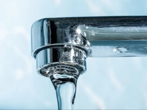 Gouttes d'eau tombant d'un robinet chromé, montrant des dépôts calcaires, un signe du tableau dureté de l'eau.