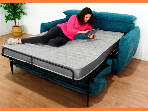 Mujer relajada en un sofá cama abierto, usando su tablet. Los sofabeds son perfectos para ahorrar espacio.