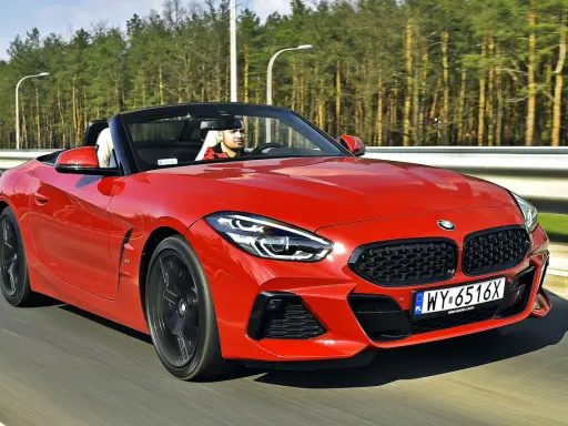 Czerwone z4 bmw z opuszczonym dachem pędzi po drodze, kierowca w czapce z daszkiem cieszy się jazdą.