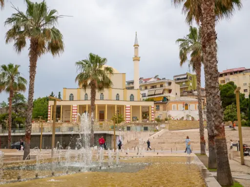 Plac z fontannami i palmami przed meczetem w Durrës, Albania. Ludzie spacerują po schodach.