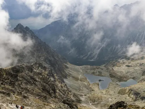 Widok na Tatry z chmurami. Szlak turystyczny prowadzi przez kamieniste zbocza do stawów. Idealne miejsce na **rysy dla początkujących**.