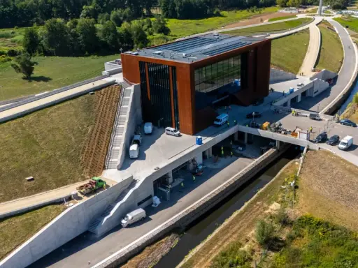 Nowoczesny budynek muzeum bitwy warszawskiej z cortenowską fasadą, otoczony zielenią i betonowymi konstrukcjami.