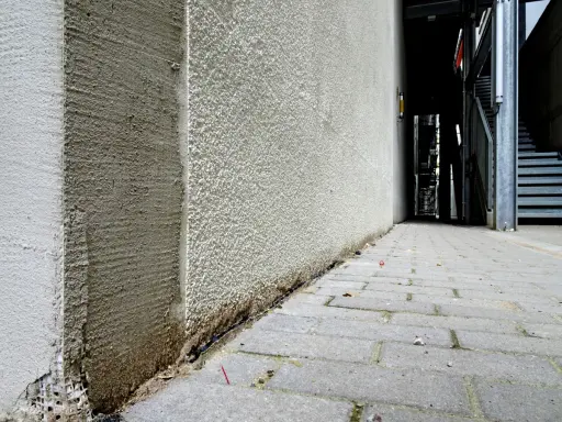 Die Ecke eines Gebäudes wird mit WDVS verputzt. Der Putz ist rau und hellgrau, mit sichtbaren Spuren der Verarbeitung.