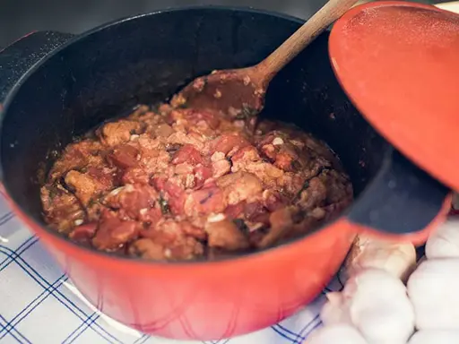 En röd gryta med en mustig toscansk tomatsoppa, en träsked rör om i den väldoftande grytan. Bredvid ligger vitlök.