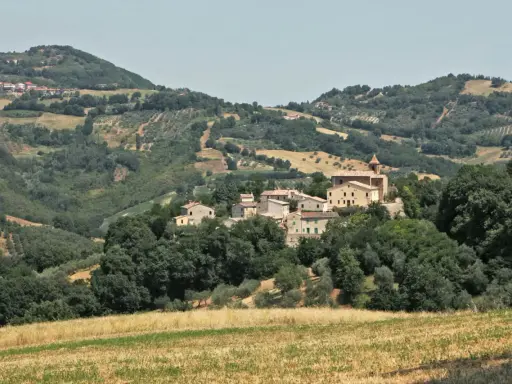 Borgo collinare di **Cerreto di Saludecio** con case in pietra e una chiesa, immerso nel verde della campagna romagnola.