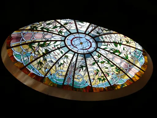 Magnifique vitrail intérieur maison, orné de fleurs roses et de motifs végétaux bleus et jaunes, illuminant la pièce.