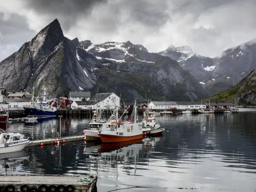 Port de pêche norvégien avec des montagnes imposantes en arrière-plan. Des bateaux de pêche sont amarrés, offrant un mouillage bateau gratuit dans ce paysage pittoresque.