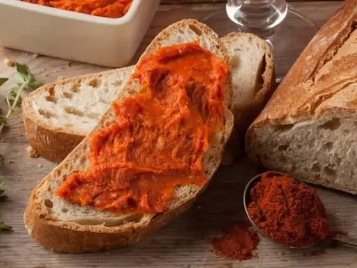 Fetta di pane con 'nduja, un assaggio di cosa mangiare in Calabria. Spezie rosse e pane fresco completano la scena.
