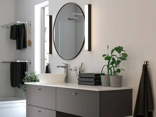 Moderno lavabo con grifería cromada, espejo ovalado y toallas negras. Ideal para una reforma de baño pequeño.