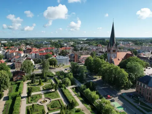 Widok z lotu ptaka na Szczecinek. Widać park miejski z fontanną, kościół z wieżą i zabudowania. To piękne **szczecinek atrakcje** turystyczne.