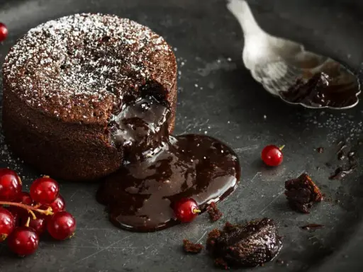 Schokoladen-Lava-Kuchen mit flüssigem Kern, bestäubt mit Puderzucker, garniert mit roten Johannisbeeren. Ein köstliches Lava Cake Rezept.