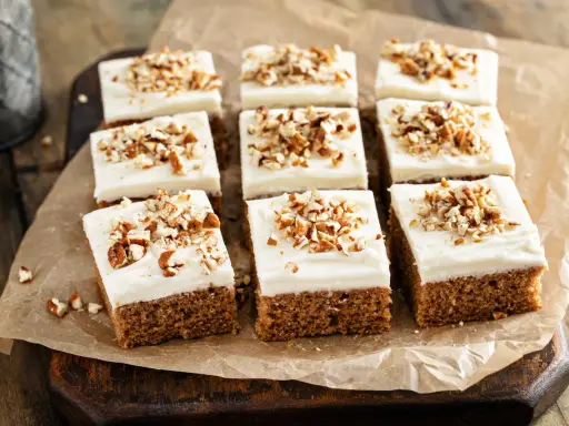 Nio bitar saftig morotskaka i långpanna med krämig frosting och hackade nötter, redo att avnjutas.