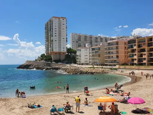 Sonniger Cullera Strand mit vielen Menschen, die sich im Meer und am Sand entspannen, im Hintergrund hohe Gebäude.