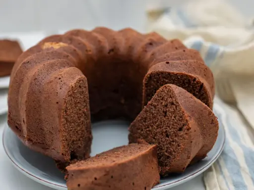 Un soffice ciambellone al cioccolato, appena sfornato, con alcune fette già pronte per essere gustate.