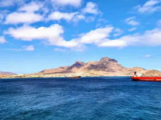 Blick auf die Bucht von Mindelo, Kap Verde, mit Schiffen im tiefblauen Wasser und einer bergigen Küstenlinie im Hintergrund.
