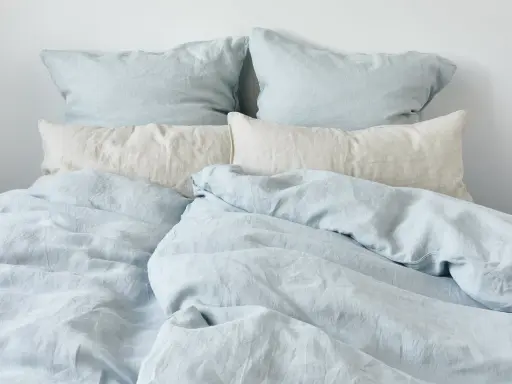 Ein Bett mit hellblauen und cremefarbenen Leinenbezügen. Perfekt für einen kühlen Sommerabend.