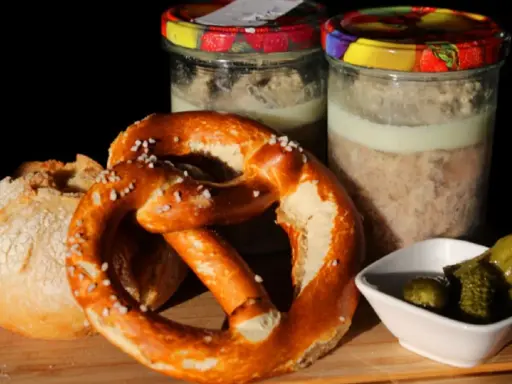 Zwei Gläser mit Fleisch einkochen im Weck-Glas, dazu ein Brezel, Brot und Gewürzgurken.
