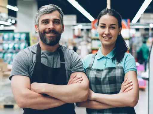 Deux employés souriants, habitués à rester debout toute la journée, posent dans un supermarché.